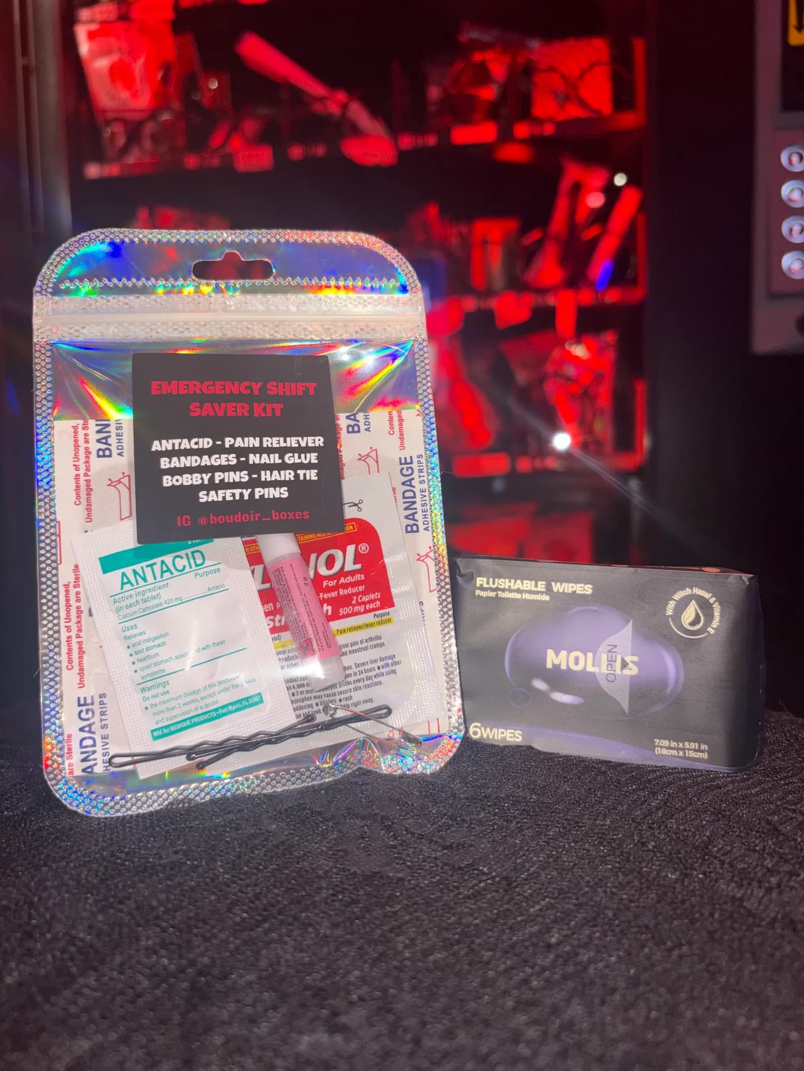 The Emergency Shift Saver Kit: antacid, pain reliever, bandages, nail glue, bobby pins, hair tie and safety pins in a holographic bag, with a pack of wipes